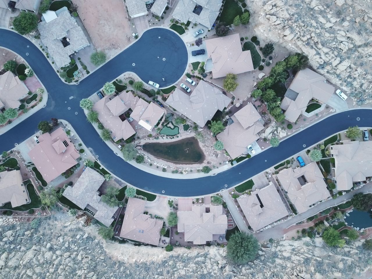 Services Drone aerial photo of a suburban neighborhood street layout with houses and greenery.